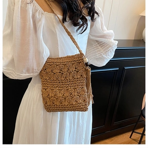 Detail of handmade straw crossbody bag with floral texture and beaded tassels on a dress