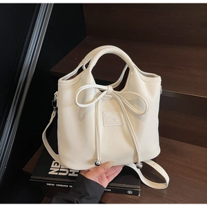 Close-up of minimalist cream white handbag with decorative ribbon bow and gold metal accents