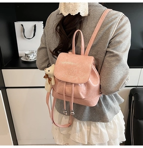 Pink patent leather bucket backpack with plush bear charm worn by a model in a stylish setting