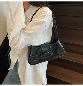 Close-up of black glossy leather underarm bag with bow detail on a casual white shirt outfit