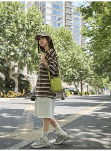 Vertical outdoor full-body shot of a student wearing a casual striped T-shirt and mini crossbody bag