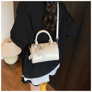 Detail of cream patent leather Boston bag with heart charm and lace bow on shoulder strap