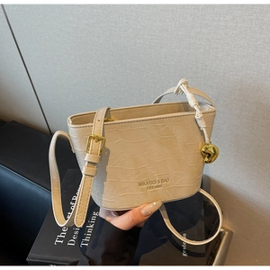 Detail of cream bucket bag showing crocodile texture and golden heart pendant accessory