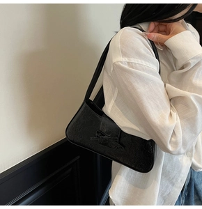 Detail of black glossy patent leather shoulder bag with pleated texture and small bow