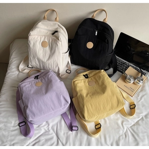 Detail of multi-colored nylon backpacks with leather handles on a white bed