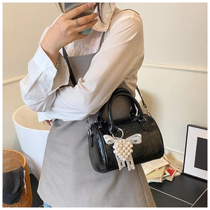Détail du sac Boston en cuir verni noir avec nœud en dentelle et pendentif en perles