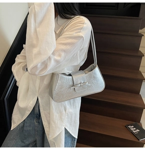 Detail of silver metallic underarm bag with pleated texture and bow buckle on shoulder