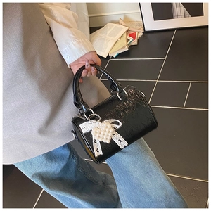 Détail du sac cylindre en cuir verni noir avec breloque cœur perle et nœud décoratif