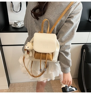 Close-up of mini cream backpack with brown flap and cute white teddy bear charm