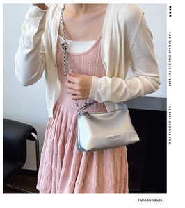 Silver glossy crossbody bag with metallic chain strap worn by model in pink dress