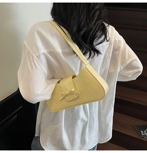 Detail view of cream pleated baguette bag with bow decoration on a shoulder