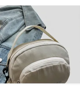 Detail of cream nylon crossbody bag featuring double zippers and a durable fabric handle