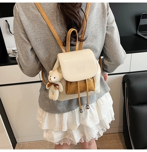 Detail of a cream bucket backpack with brown trim and cute teddy bear charm on back