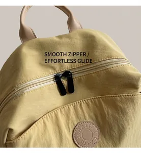 Detail of smooth black double zippers and TUMAITU logo on beige nylon backpack