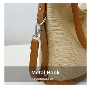 Detail of woven straw bag showing silver metal spring hooks and brown leather strap