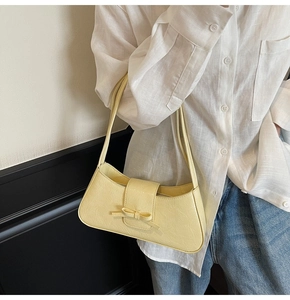 Close-up of cream underarm bag with bow detail worn by model in casual outfit