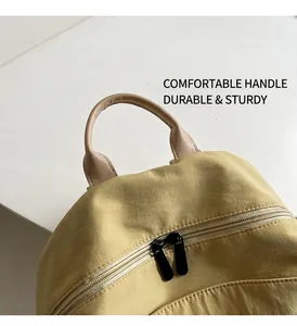 Detail of tan leather handle and black dual zippers on beige nylon backpack top
