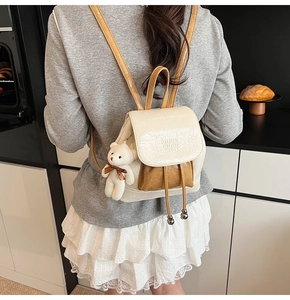 Close-up of cream and brown mini bucket backpack with cute plush bear charm on model