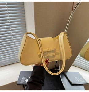 Detail of light yellow embossed leather underarm bag featuring a cute bow decoration