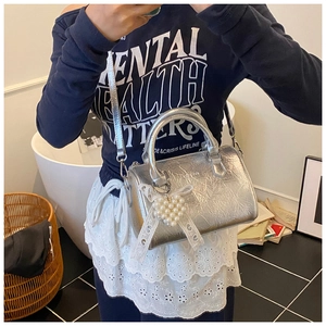 Detail of silver pleated texture handbag with lace bow and pearl heart charm accessory