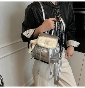 Detail of silver metallic bucket backpack with crinkled texture and plush bear charm