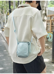 Close-up of light blue wrinkled nylon crossbody bag with dual zip pockets on model