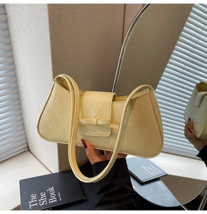 Close-up of cream underarm bag featuring vintage pleated texture and a bow detail