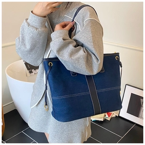 Détail d'un grand sac cabas en denim avec surpiqûres blanches et œillets métalliques