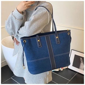 Blue denim tote bag with white contrast stitching and gold metal hardware shown on model