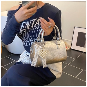 Détails d'un sac cylindre argenté avec texture froissée et breloque cœur perle