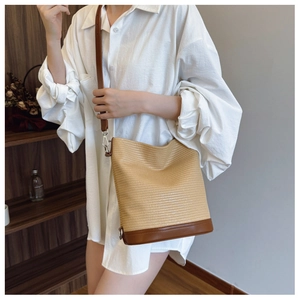 Detail of woven straw bucket bag with dark brown leather base and adjustable shoulder strap
