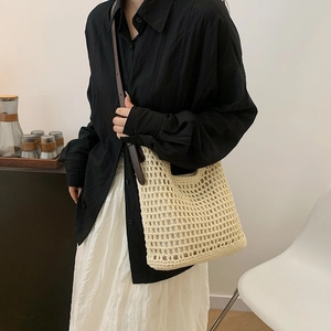 Detail of a beige woven tote bag with brown leather straps worn by a model