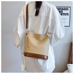 Detail of light khaki woven bucket bag with brown leather base on a shoulder strap
