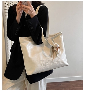 Detail of cream tote bag with letter embossing and cute bear charm in a chic interior