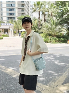 Light blue nylon crossbody bag with drawstring closure shown in an outdoor street setting
