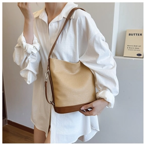 Detail of woven straw bucket bag with brown leather base and adjustable shoulder strap