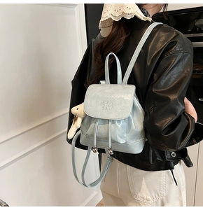 Detail of light blue mini backpack with textured shiny leather and plush bear charm
