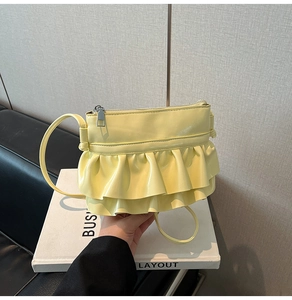 Detail of pale yellow patent leather shoulder bag with ruffled layers and silver zipper