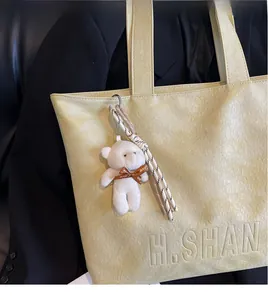Detail of light beige tote bag with embossed pattern and plush bear charm decoration
