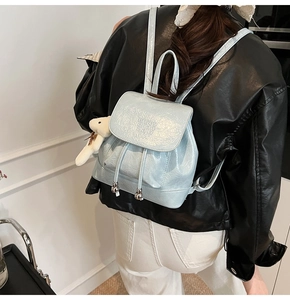 Blue patent leather mini backpack with plush bear charm worn on a black leather jacket