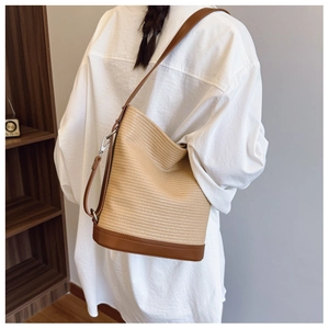 Detail of woven straw bucket bag with brown leather trim and adjustable shoulder strap