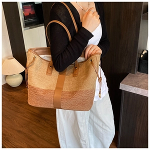 Detail of large tote bag in woven fabric with brown leather straps and drawstring accents