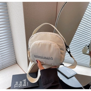 Detail of off-white canvas crossbody bag featuring front zipper pocket and wide strap