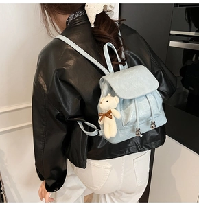 Detail of light blue bucket backpack with crinkled finish and plush bear charm decoration