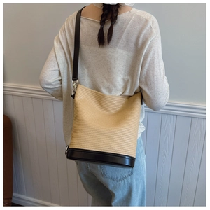 Model view of a handwoven straw bucket bag with black leather base and shoulder strap