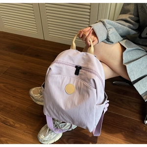 Detail of light purple lightweight travel backpack with a circular badge on wood floor