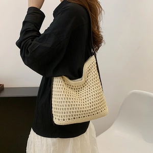 Detail view of beige woven tote bag with brown leather straps on woman's shoulder