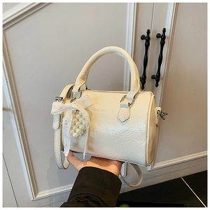 Détail du sac cylindrique blanc crème avec nœud en dentelle et pendentif en perles