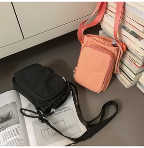 Detailed view of dual-layer nylon crossbody bags in black and coral pink with zip pockets