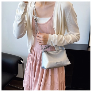 Close-up of a metallic silver crossbody bag with a decorative knotted chain strap detail